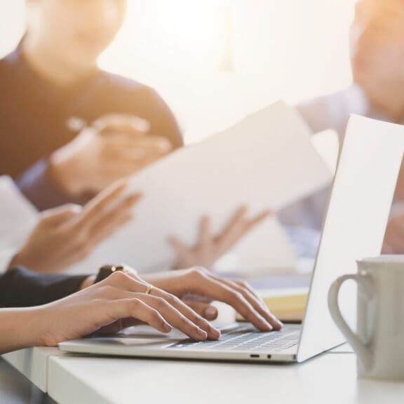 Close up view of business people typing on computer laptop while working with her team in simple meeting room