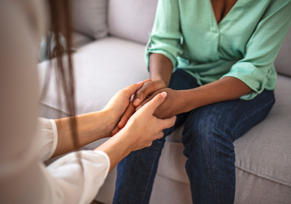Close up African American psychotherapist holding clipboard, touching patient hands, expressing empathy and support at meeting, counselor therapist comforting girl during personal therapy session